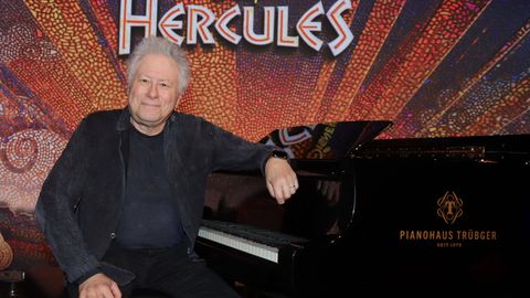 Komponist Alan Menken sitzt an einem Flügel und guckt in die Kamera, hinter ihm steht der Schriftzug Hercules