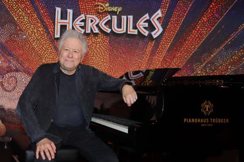 Komponist Alan Menken sitzt an einem Flügel und guckt in die Kamera, hinter ihm steht der Schriftzug Hercules