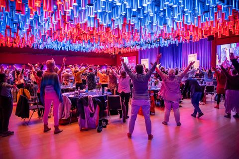 650 Menschen in einem großen Saal strecken auf dem Engelkongress die Hände Richtung Himmel.