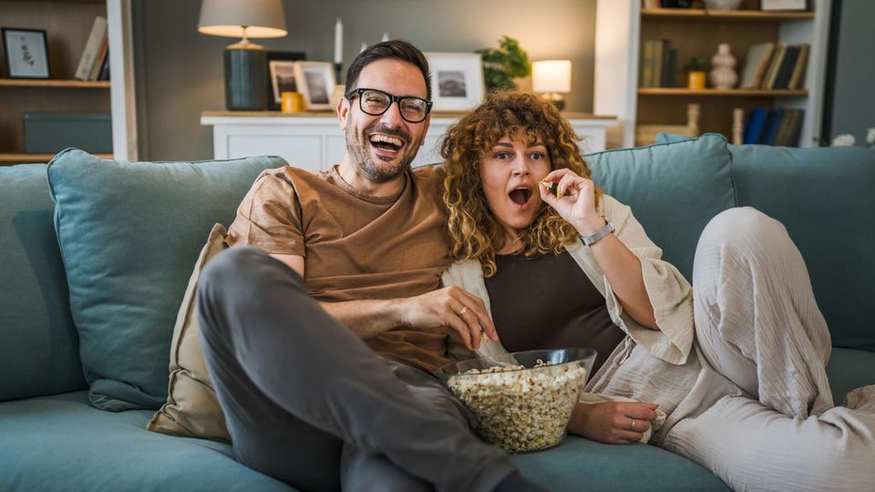 Pärchen genießt einen Fernsehabend auf dem heimischen Sofa und isst dabei Popcorn