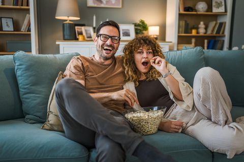 Pärchen genießt einen Fernsehabend auf dem heimischen Sofa und isst dabei Popcorn