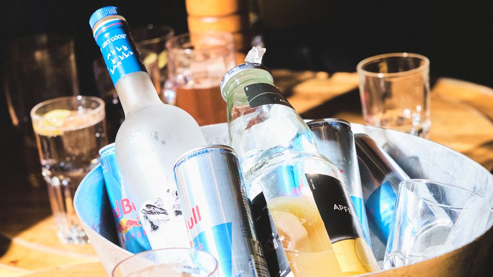 Nahaufnahme eines Kühlers voll mit Wodka und Redbull auf einem Tisch mit vollen Gläsern