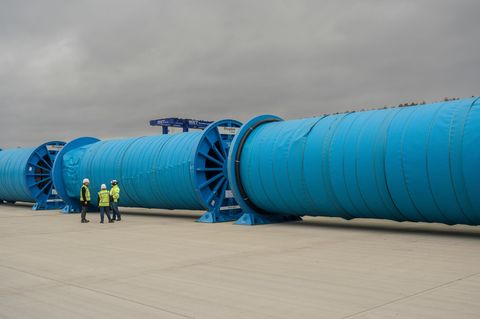 Energiewende: Aufgerollte Kupferkabel. Davor stehen drei Menschen, die klein wirken im Vergleich
