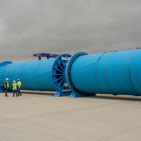 Energiewende: Aufgerollte Kupferkabel. Davor stehen drei Menschen, die klein wirken im Vergleich