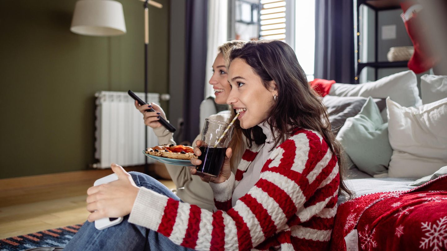 Zwei Frauen sitzen vor einer Couch und schauen gebannt Fernsehen mit dem Waipu.TV-Angebot.