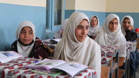 An drei Tischen sitzen jeweils zwei afghanische Mädchen mit weißen Kopftüchern.