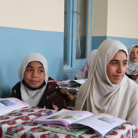 An drei Tischen sitzen jeweils zwei afghanische Mädchen mit weißen Kopftüchern.