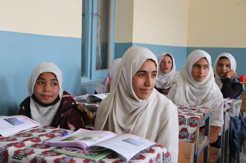 An drei Tischen sitzen jeweils zwei afghanische Mädchen mit weißen Kopftüchern.