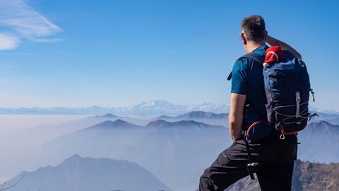 Ein Mann steht auf einem Berggipfel und blickt auf den Horizont