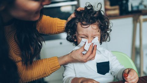 Erkältung und Nase schnäuzen: Eine Frau hilft einem Kind beim Schnäuzen