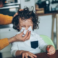 Erkältung und Nase schnäuzen: Eine Frau hilft einem Kind beim Schnäuzen