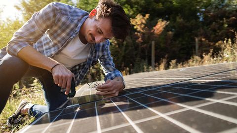 Mann schraubt im Garten an einem Solarpaneel, um einen Solartisch zu bauen.