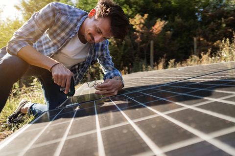 Mann schraubt im Garten an einem Solarpaneel, um einen Solartisch zu bauen.