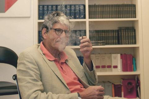 Rupert von Plottnitz sitzt in einem Stuhl und raucht eine Zigarette.