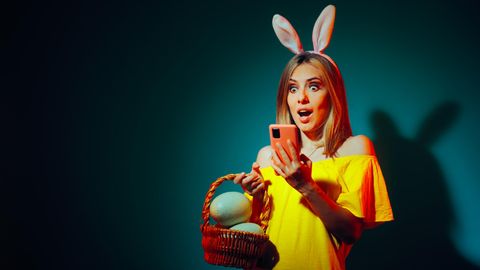 Frau mit gelbem Oberteil und Häschenohren schaut erstaunt auf ihr Smartphone