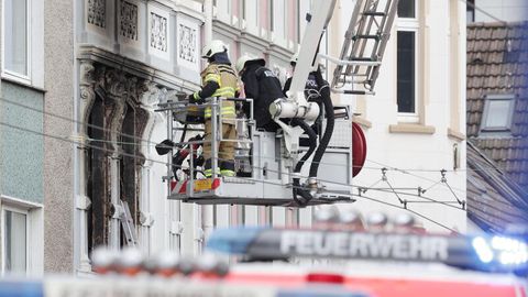 Solingen: Feuerwehrmänner stehen vor einem Mehrfamilienhaus, in dem es gebrannt hat, im Korb einer Drehleiter