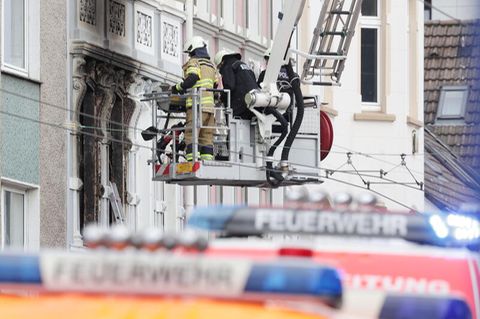 Solingen: Feuerwehrmänner stehen vor einem Mehrfamilienhaus, in dem es gebrannt hat, im Korb einer Drehleiter