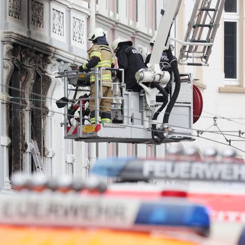 Solingen: Feuerwehrmänner stehen vor einem Mehrfamilienhaus, in dem es gebrannt hat, im Korb einer Drehleiter