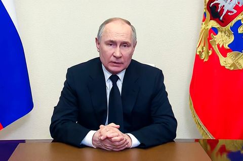 Wladimir Putin sitzt zwischen zwei russischen Flaggen an einem Schreibtisch