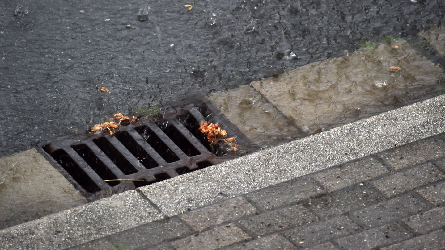 Nahaufnahme eines Gullideckels, in den Regenwasser reinrauscht.
