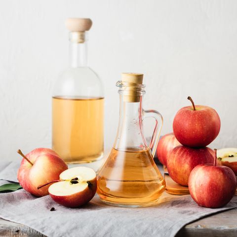 Apfelessig: Zwei Flaschen mit Apfelessig stehen auf einem Tisch, daneben liegen Äpfel