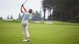 Eine Golfspielerin schlägt mit ihrem Schläger nach dem Golfball auf dem Platz.