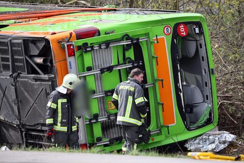 Ein hellgrüner Bus liegt auf der A9 bei Leipzig auf der Seite, während zwei Feuerwehrleute an seinem Heck stehen
