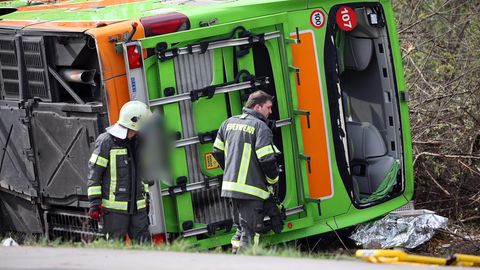 Ein hellgrüner Bus liegt auf der A9 bei Leipzig auf der Seite, während zwei Feuerwehrleute an seinem Heck stehen
