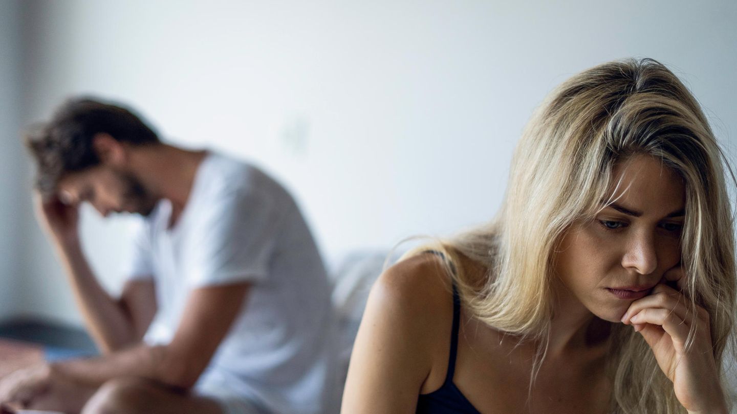 Ein Paar sitzt nach einem Streit auf einem Bett beide schauen traurig und verzweifelt in entgegengesetzte Richtungen