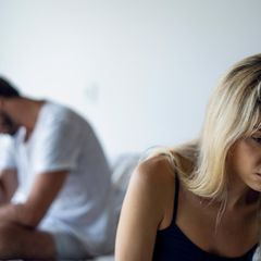 Ein Paar sitzt nach einem Streit auf einem Bett beide schauen traurig und verzweifelt in entgegengesetzte Richtungen