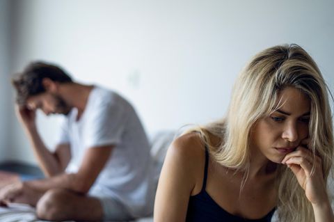Ein Paar sitzt nach einem Streit auf einem Bett beide schauen traurig und verzweifelt in entgegengesetzte Richtungen
