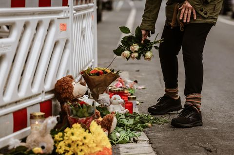 Eine Frau legt Blumen an die Absperrung vor einem Wohnhaus in Solingen nieder, in dem eine komplette Familie ums Leben kam