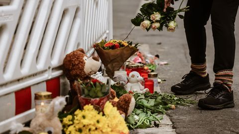 Eine Frau legt Blumen an die Absperrung vor einem Wohnhaus in Solingen nieder, in dem eine komplette Familie ums Leben kam