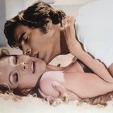 Ein Mann liegt auf einer Frau und küsst ihre Wange, während sie sich weggedreht hat, den Mund halb geöffnet.