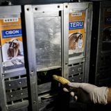 Eine behandschuhte Hand steckt durch einen Schlitz eine Banane in eine der Transportkisten