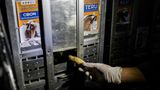 Eine behandschuhte Hand steckt durch einen Schlitz eine Banane in eine der Transportkisten