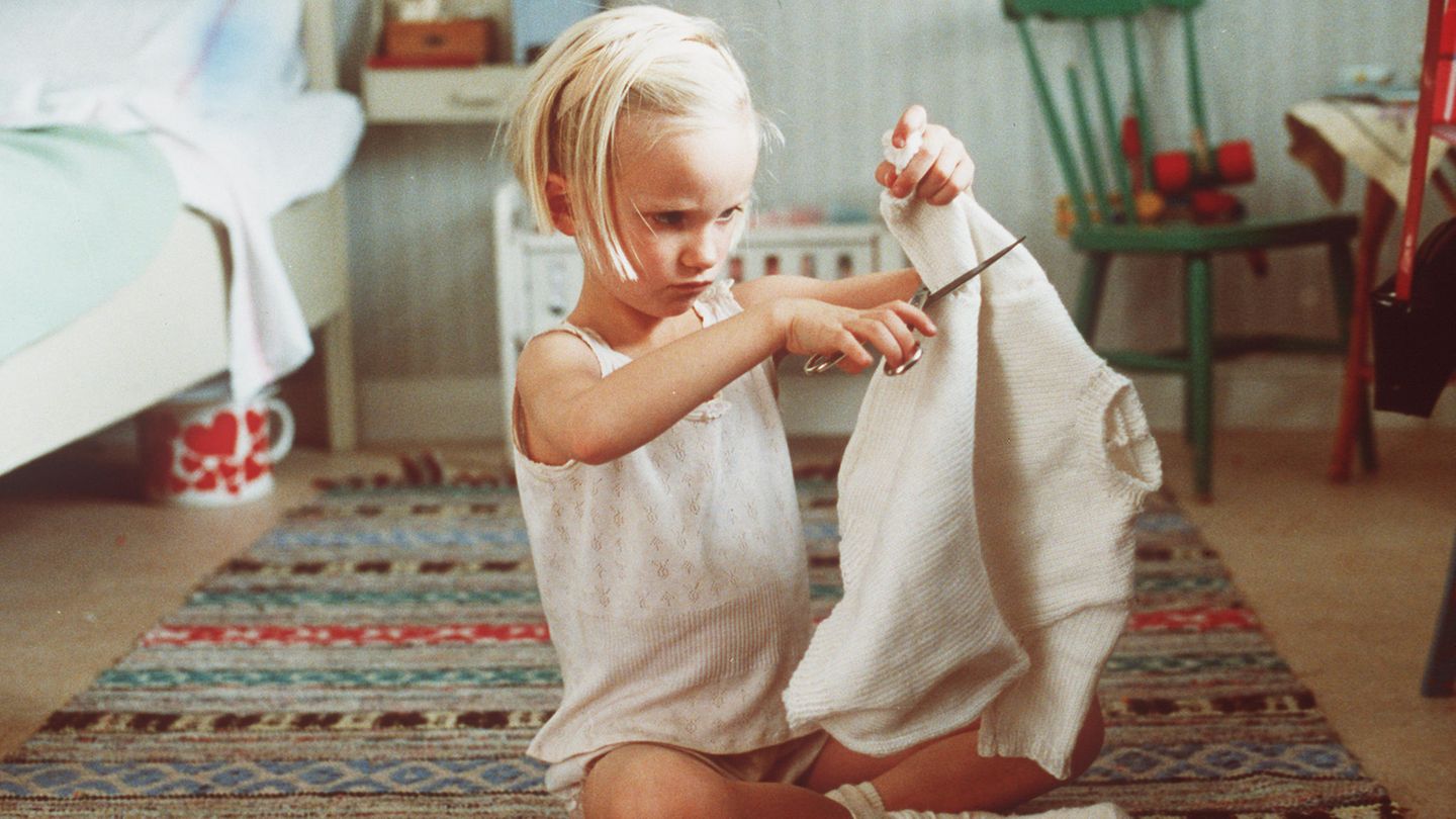 Lotta zieht um Ein fünfjähriges Mädchen im Unterhemd sitzt im Schneidersitz auf dem Boden und zerschneidet einen Pullover.