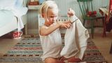 Ein fünfjähriges Mädchen im Unterhemd sitzt im Schneidersitz auf dem Boden und zerschneidet einen Pullover.