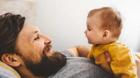 Baby liegt auf der Brust des Vaters, beide sehen sich in die Augen