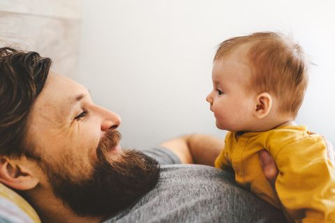 Baby liegt auf der Brust des Vaters, beide sehen sich in die Augen