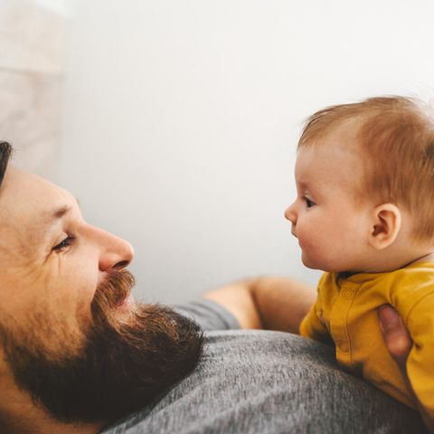 Baby liegt auf der Brust des Vaters, beide sehen sich in die Augen