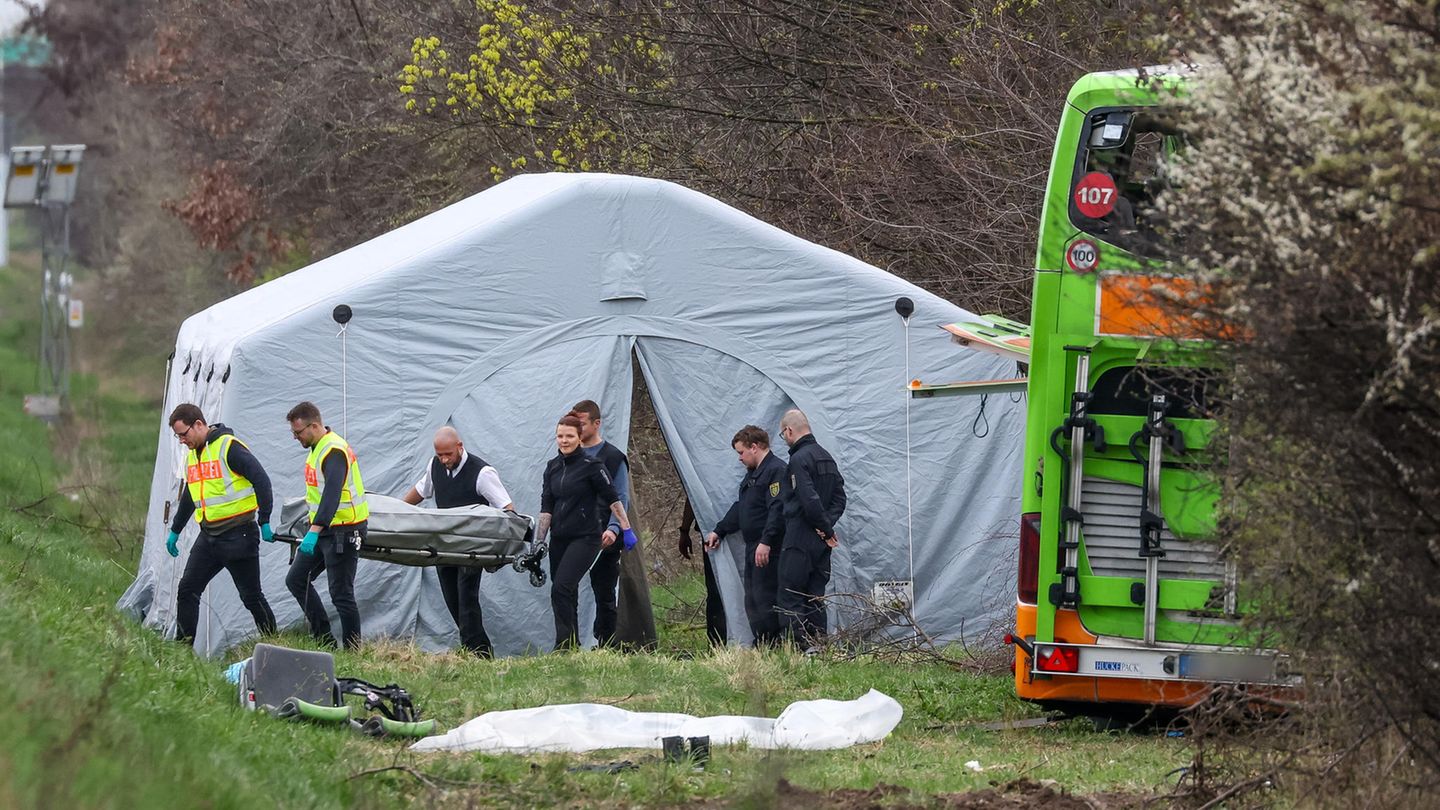 An der A9 steht ein grüner Reisebus nach einem Busunglück zerstört an der Böschung