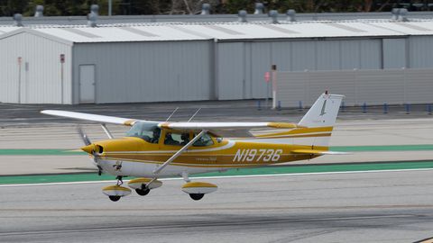 Eine goldgelb und weiß lackierte Cessna 172 fliegt tief über einer Start- und Landebahn