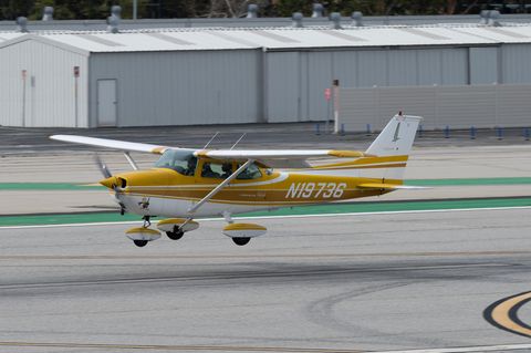 Eine goldgelb und weiß lackierte Cessna 172 fliegt tief über einer Start- und Landebahn