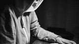 Janne im Profil an ihrem Laptop, nur Nase und Kinn sieht man unter der Hoodie Kapuze.