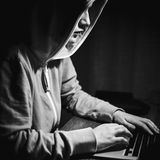 Janne im Profil an ihrem Laptop, nur Nase und Kinn sieht man unter der Hoodie Kapuze.