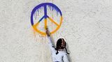 Ein Graffiti von einem Kind. Das Kind malt ein Peace Zeichen in ukrainischen Flaggenfarben an die Wand