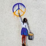 Ein Graffiti von einem Kind. Das Kind malt ein Peace Zeichen in ukrainischen Flaggenfarben an die Wand