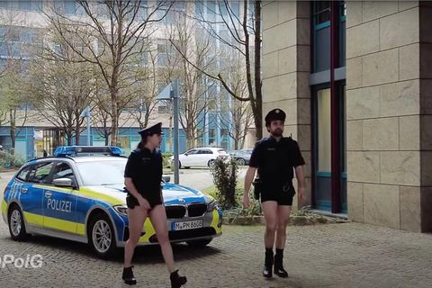 Zwei Polizisten gehen ohne Hosen vor einem Streifenwagen