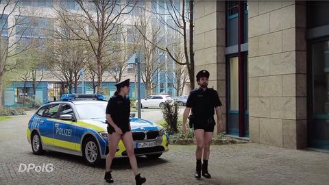 Zwei Polizisten gehen ohne Hosen vor einem Streifenwagen